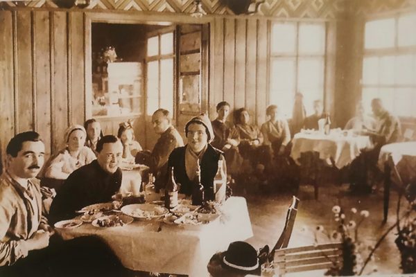 zdjęcie kolorze sepii, lata czterdzieste, widać ludzi siedzących przy stolikach w drewnianym schronisku